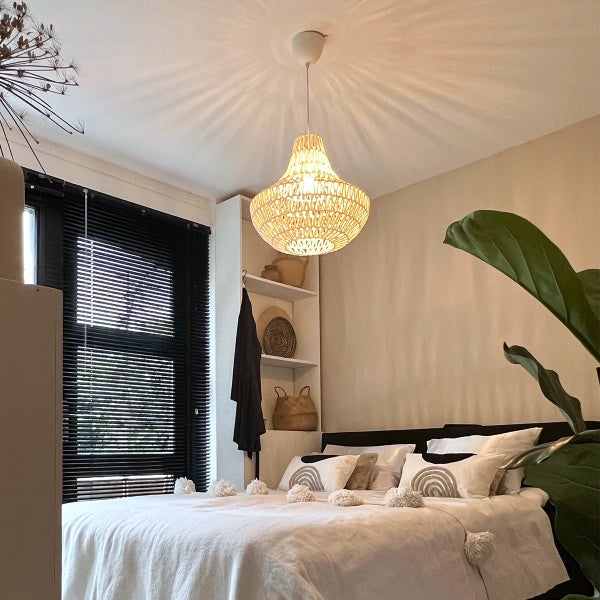 Gemütliches Schlafzimmer im Boho-Stil mit Rattan-Pendelleuchte über einem Bett mit weißer Bettwäsche, dunklen Jalousien und Regal.