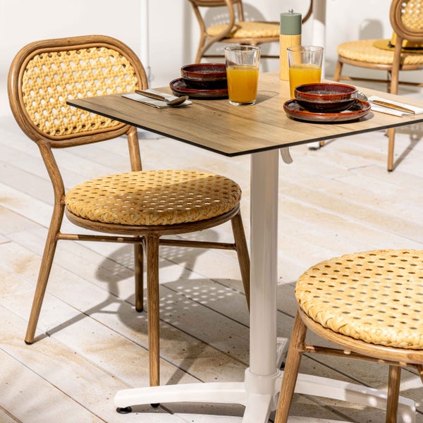 Modernes Gartenmöbel-Set bestehend aus quadratischem Tisch in Holzoptik und passenden Flechtstühlen auf einer Holzterrasse.