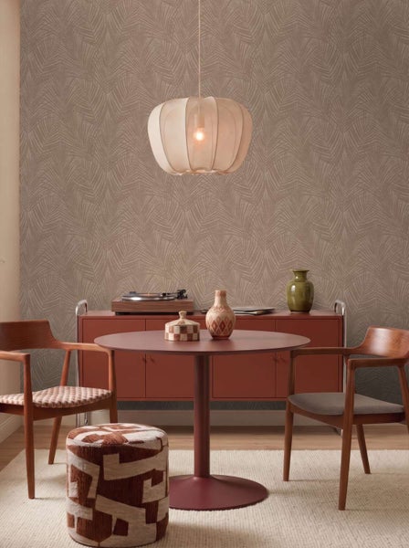 Wohnzimmer mit Vliestapete mit Palmblattmuster, runder Esstisch, Holzstühle, dekorativer Hocker und Pendelleuchte in einem modernen Einrichtungsstil.