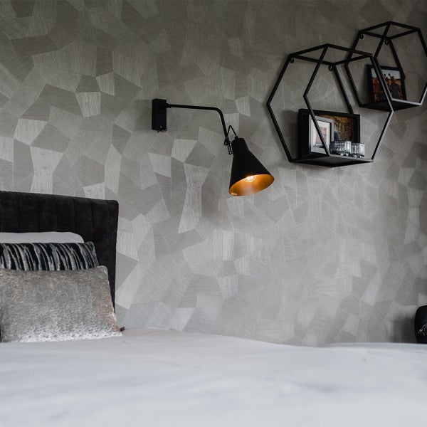 Modernes Schlafzimmer mit geometrischer Tapete, verstellbarer Wandleuchte und schwarzen sechseckigen Wandregalen mit Dekorationsartikeln.