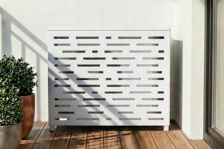 Weiße Klimaanlagen-Abdeckung aus Metall mit horizontalem Schlitzmuster für die Außeneinheit auf einem Holzbalkon neben einer Pflanze.