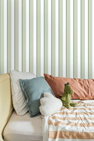 Dekoratives Schlafzimmer mit gestreifter Tapete, Kissen und Stofftier auf dem Bett