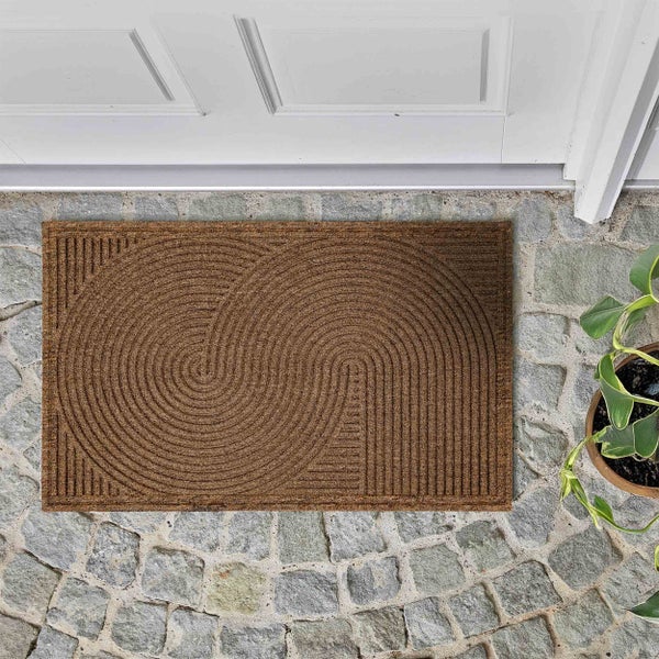 Rechteckige Kokos-Fußmatte mit geometrischem Rillenmuster aus konzentrischen Halbkreisen vor einer weißen Eingangstür auf Steinboden.