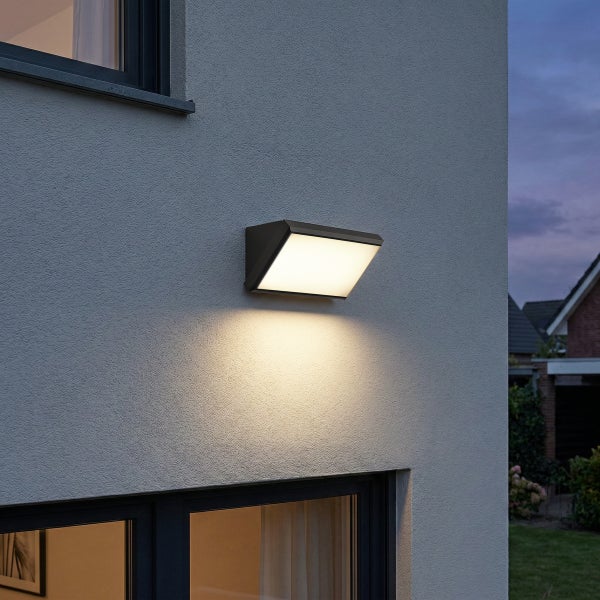 Moderne LED Außenwandleuchte an einer Hausfassade montiert, die warmweißes Licht nach unten abstrahlt.