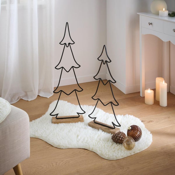 Zwei dekorative Weihnachtsbaum Silhouetten aus Metall auf Holzsockel auf einem Fellteppich mit Tannenzapfen und Dekokugeln.