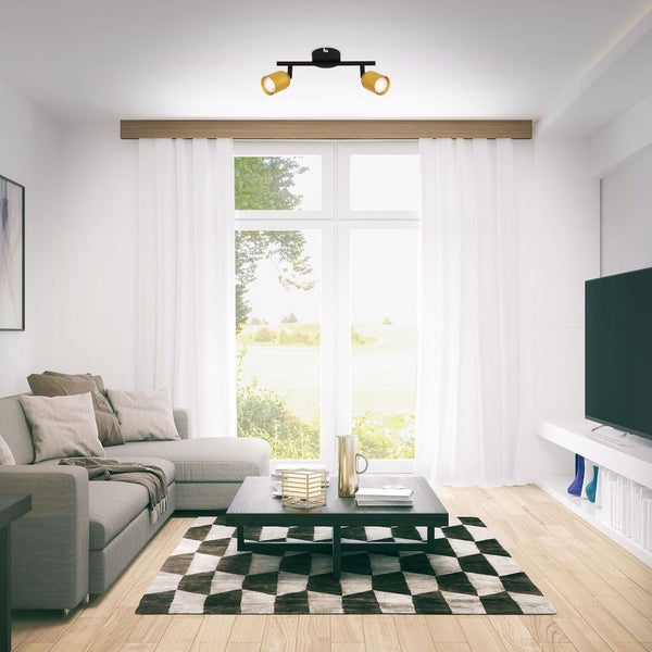 Moderner, heller Wohnraum mit grauem Ecksofa, dunklem Couchtisch auf einem karierten Teppich und einem zweiflammigen Deckenstrahler.