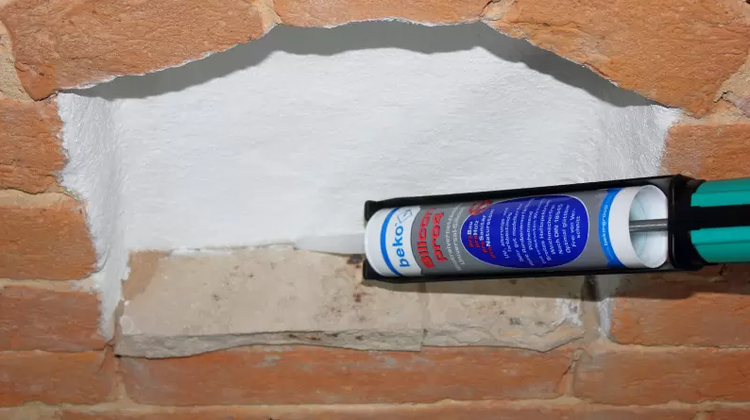 Eine Kartusche mit Dichtstoff wird in eine Mauernische appliziert.