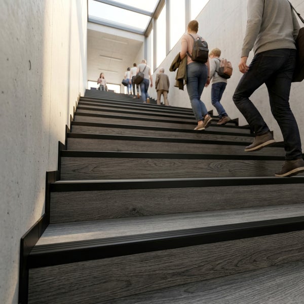 Moderne Treppenrenovierung mit Stufen in Holzoptik und schwarzen Treppenkantenprofilen in einem hellen Treppenhaus mit Sichtbetonwänden.
