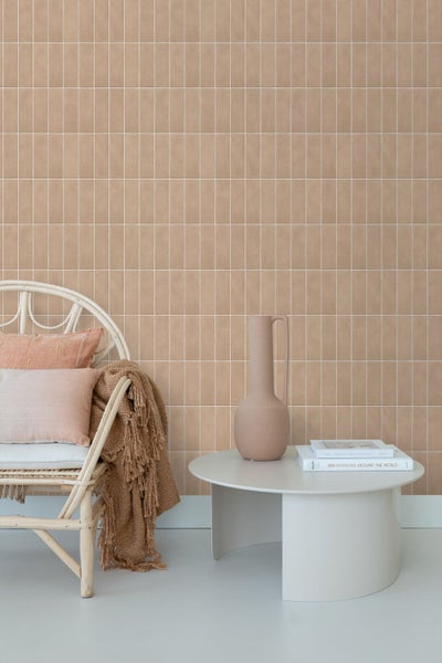 Wand mit rechteckigen Fliesen im Hochformat, Rattan Sessel mit Kissen, Beistelltisch mit Vase und Buchtiteln in einem modernen Wohnraum.