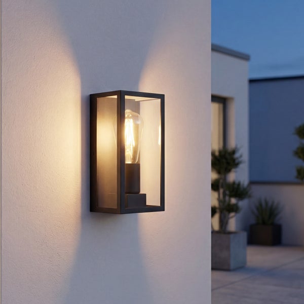 Rechteckige Außenwandleuchte aus schwarzem Metall und Glas mit warmem Lichtschein nach oben und unten an einer hellen Fassade.