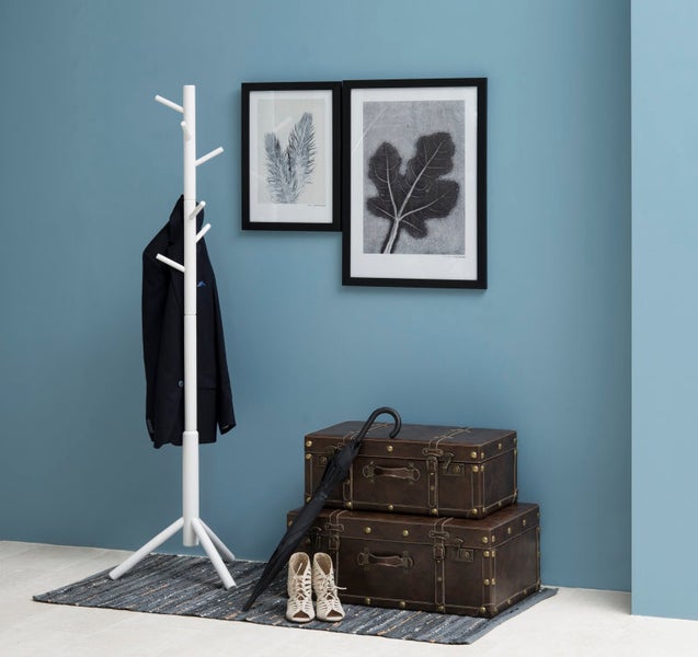 Moderner, organisierter Flur mit weißem Holzkleiderständer, Sakko, zwei braunen Vintage-Truhen, Regenschirm und Wandbildern.