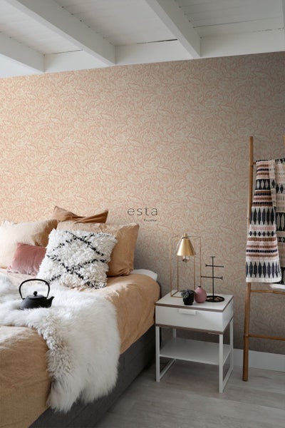 Schlafzimmer mit floral gemusterter Tapete, Bett mit Dekokissen, flauschigem Überwurf und weißem Nachttisch. esta home Logo.