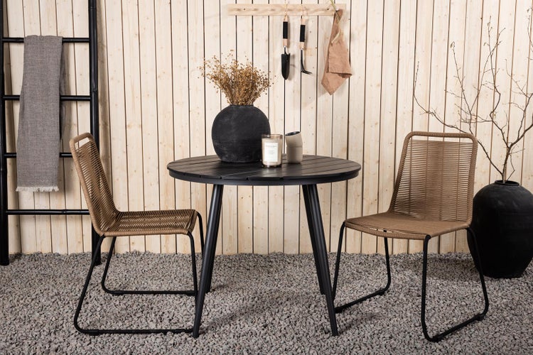 Gartenszene mit schwarzem runden Tisch, zwei Rattanstühlen und dekorativen Elementen