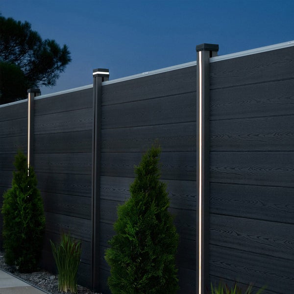 Sichtschutzzaun aus WPC in Anthrazit mit Holzmaserung und integrierter LED-Beleuchtung an den Zaunpfosten in einem Garten bei Nacht.