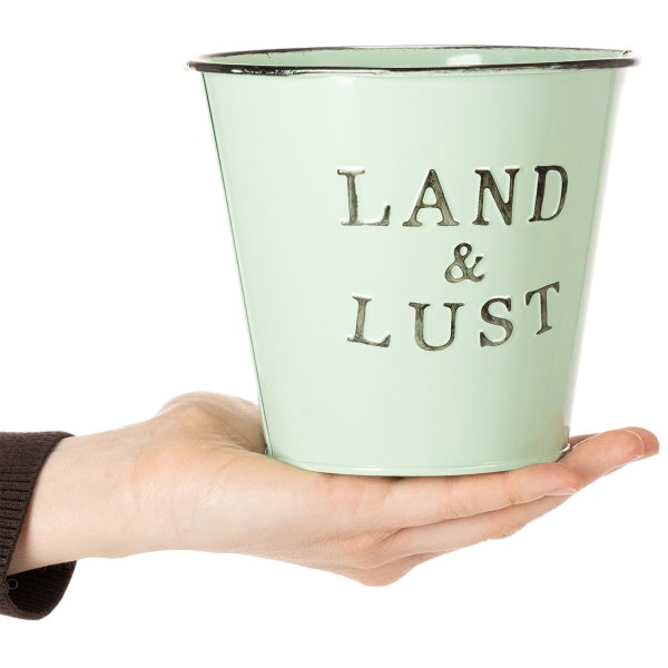 Kleiner Übertopf aus Metall in Hellgrün mit geprägtem Schriftzug LAND und LUST in einer Hand.