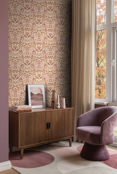 Wohnzimmer mit Vliestapete im floralen Design, einem Sideboard aus Holz, einem Polstersessel und einem Teppich mit Kreismuster vor einem Fenster.