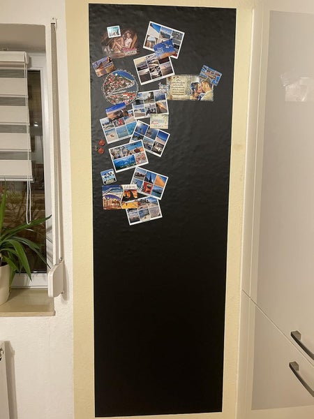 Großflächige schwarze Magnetwand mit verschiedenen Fotos und Postkarten, die mit Magneten befestigt sind.
