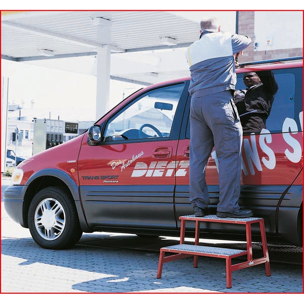 Eine Person steht auf einer zweistufigen Arbeitsbühne vor einem Auto.