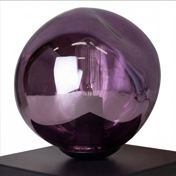 Lilafarbene Tischleuchte aus Glas in unregelmäßiger Kugelform mit sichtbarem Leuchtmittel auf schwarzem Sockel.