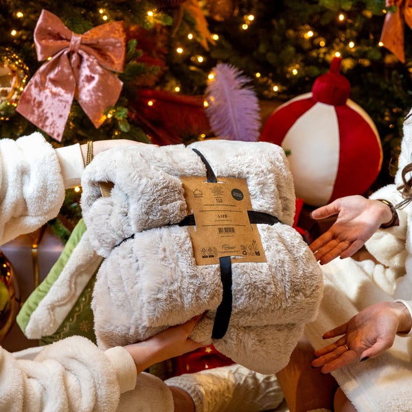 Flauschedecke mit Banderole vor einem Weihnachtsbaum