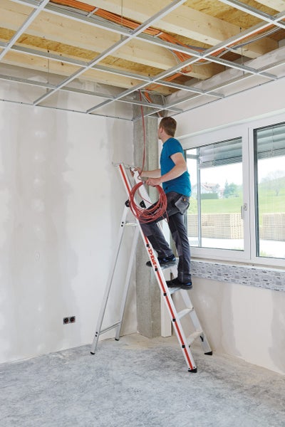Handwerker auf einer Leiter bei Elektroinstallationen in einem Rohbau.