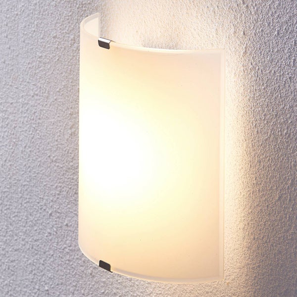 Wandleuchte aus gebogenem, satiniertem Glas mit Halteklammern aus Metall und warmem Lichtschein auf verputzter Wand.