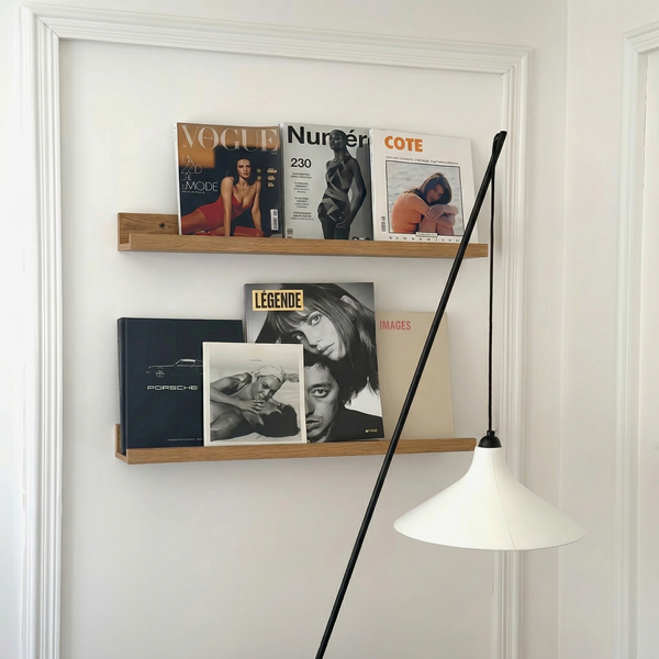 Zwei Wandregale aus Holz an einer weißen Wand mit Zeitschriften und Büchern sowie eine moderne Stehlampe im Vordergrund.