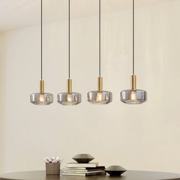 Vierflammige Pendelleuchte mit zylindrischen Schirmen aus Rauchglas und goldfarbenen Metallfassungen über einem Tisch.