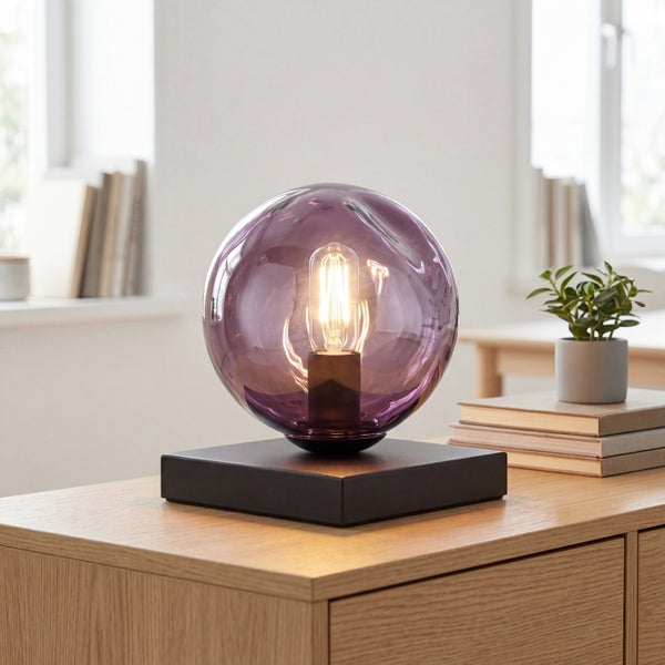 Moderne Tischleuchte mit lila Glaskugel und quadratischem schwarzem Sockel sowie sichtbarem Leuchtmittel.