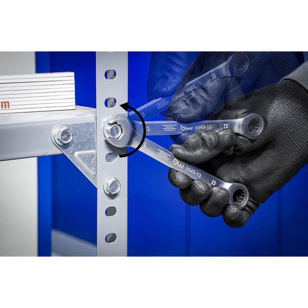 Ein Mann mit Arbeitshandschuhen dreht eine Schraube an einem Regal mit einem Ringratschenschlüssel.