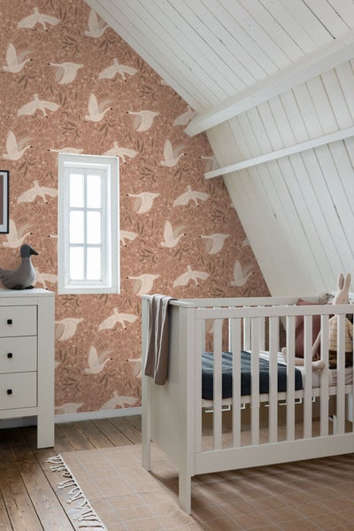 Kinderzimmer mit gemusterter Tapete, weißer Kommode und Gitterbett