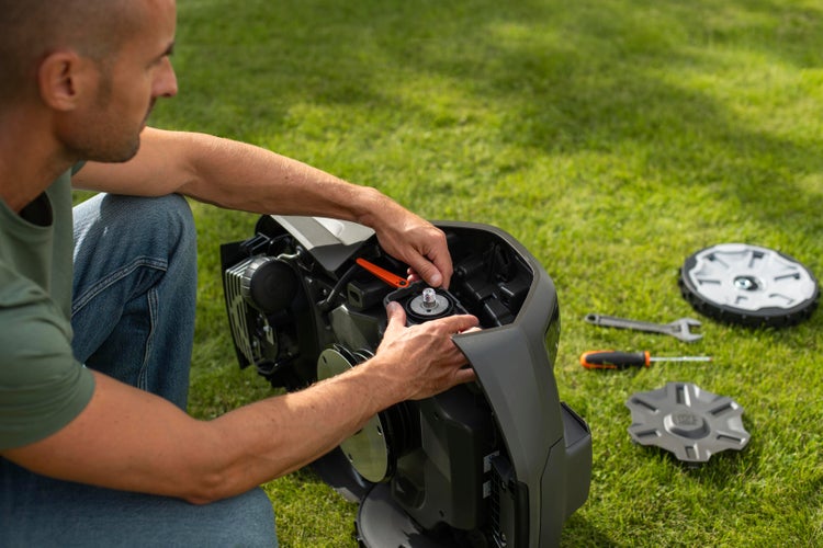 Mann wartet einen Rasenmähroboter auf einer Rasenfläche.