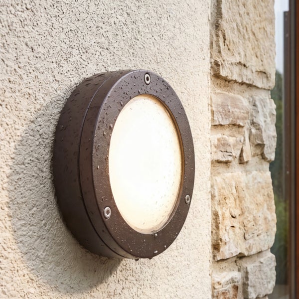 Runde, dunkelbraune Außenwandleuchte aus Metall mit weißem Glasdiffusor, eingeschaltet an einer Hauswand.