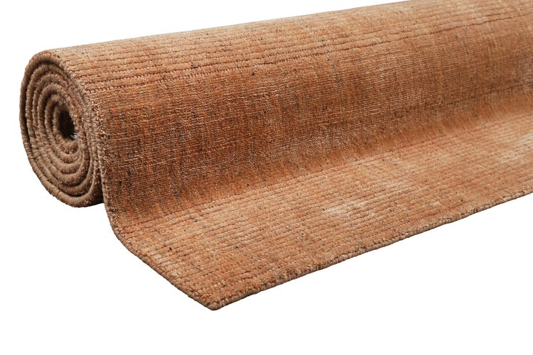 Rechteckiger Teppich mit strukturierter, gerippter Oberfläche vor einem modernen Sofa mit verschiedenen gemusterten Dekokissen.