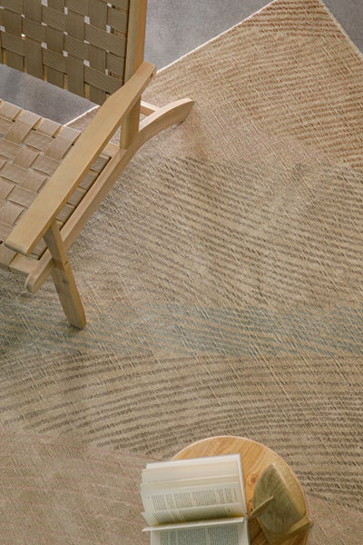 Strukturierter Teppich mit dezentem Streifenmuster in einem hellen Wohnbereich mit Holzstuhl mit Geflecht und einem Beistelltisch mit einem Buch.