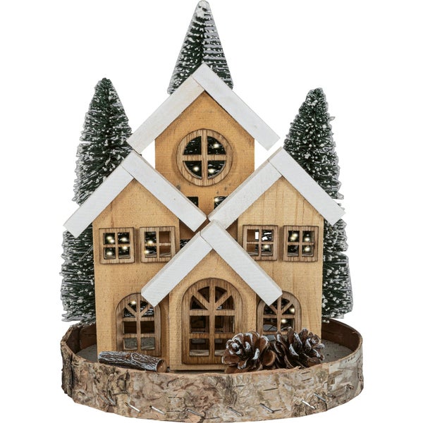 Beleuchtetes Holzhaus als Weihnachtsdekoration auf einem Holzsockel mit Tannenbäumen und Tannenzapfen.