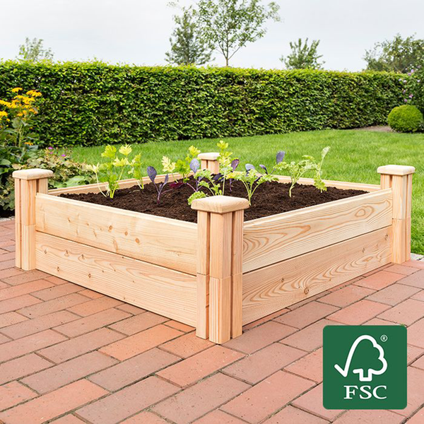 Hochbeet aus Holz mit Erde und jungen Pflanzen auf einer gepflasterten Terrasse im Garten. FSC-zertifiziertes Holz.