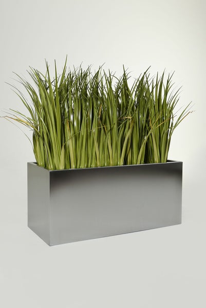 Künstliches Gras in einem rechteckigen silberfarbenen Pflanzgefäß aus Metall.