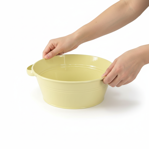 Gelbe runde Zinkschale mit zwei Henkeln, von zwei Händen gehalten.