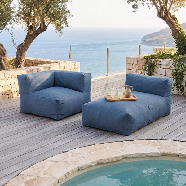 Blaue Outdoor-Loungemöbel auf einer Holzterrasse mit Pool, Steinmauer und Olivenbäumen mit Blick auf das Meer.