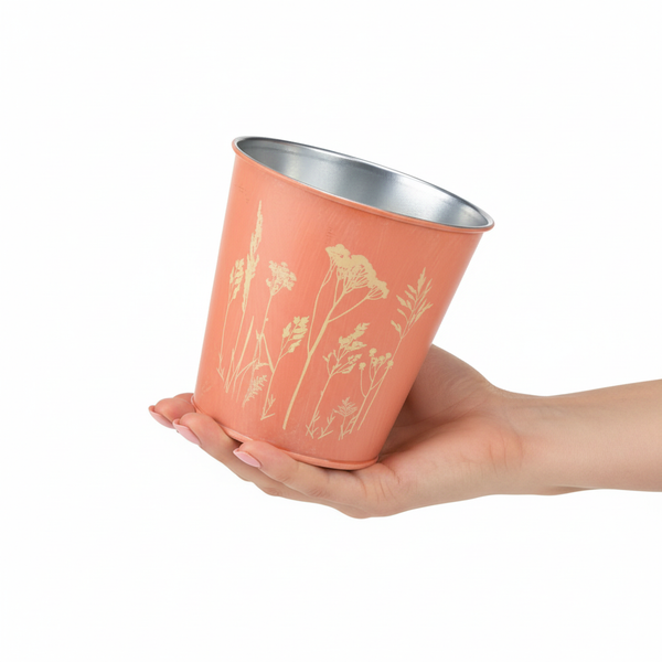 Kleiner lachsfarbener Übertopf aus Metall mit floralem Muster, in einer Hand zur Größendarstellung.