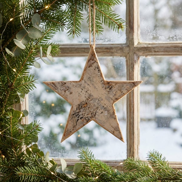 Weihnachtsstern Dekoration aus Birkenholz mit Aufhänger vor einem Fenster mit Tannenzweigen.