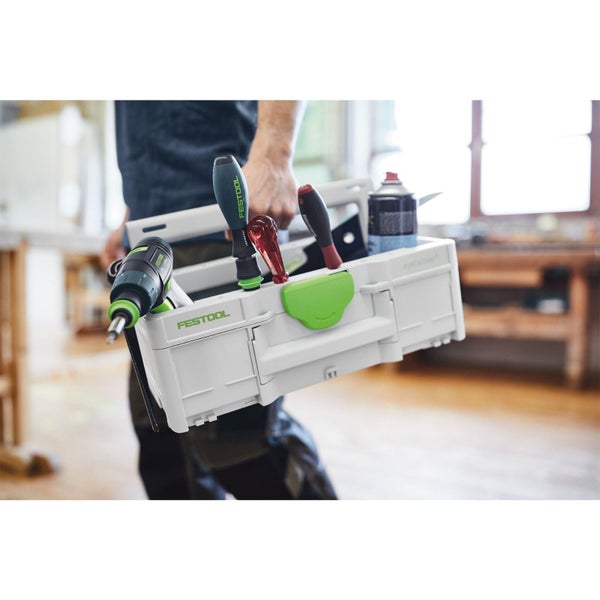 Eine Person trägt eine Festool Systainer Werkzeugbox mit Festool Logo, einem Akkuschrauber und Handwerkzeugen in einer hellen Werkstatt.
