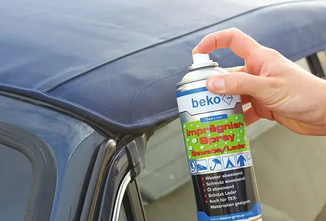 Hand die eine Dose beko Imprägnierspray für Gewebe und Leder auf ein Cabrioverdeck sprüht.