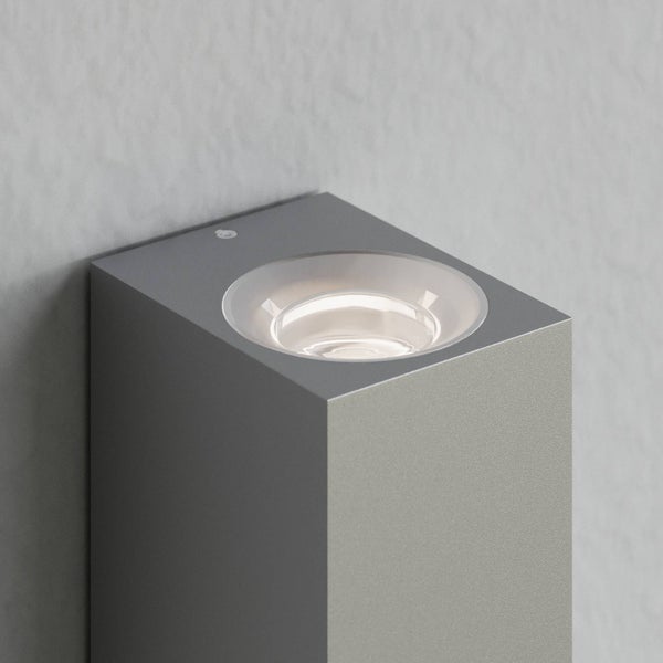 Moderne, graue Außenwandleuchte in rechteckiger Form mit integrierter, runder Lichtquelle auf der Oberseite.