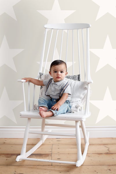 Kleinkind sitzt auf einem weißen Schaukelstuhl vor einer Wand mit Sternmuster
