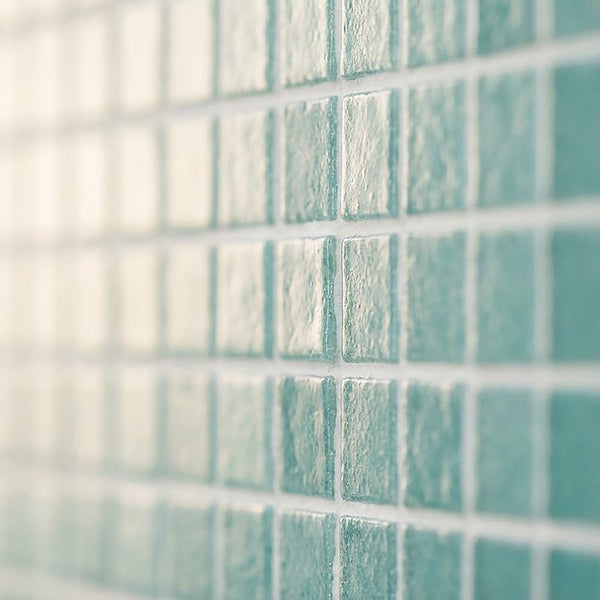 Nahaufnahme von quadratischen Mosaikfliesen mit strukturierter Oberfläche zur Wandgestaltung in einem Badezimmer.