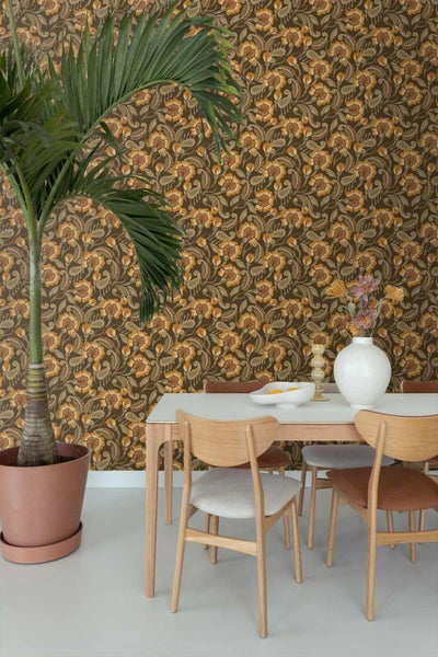 Esszimmer mit floral gemusterter Tapete, einem Esstisch aus Holz mit Stühlen und einer großen Zimmerpalme.