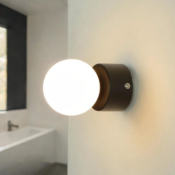 Wandleuchte mit runder, leuchtender Kugel und dunkler Halterung an der Wand