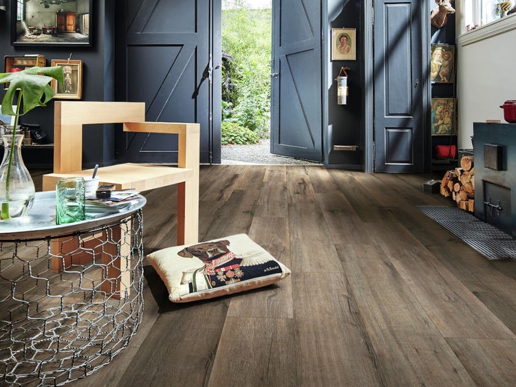 Wohnraum mit rustikalem Laminatboden in Holzoptik, dunkle Flügeltüren führen in einen Garten, moderne Holzmöbel und ein Kaminofen.